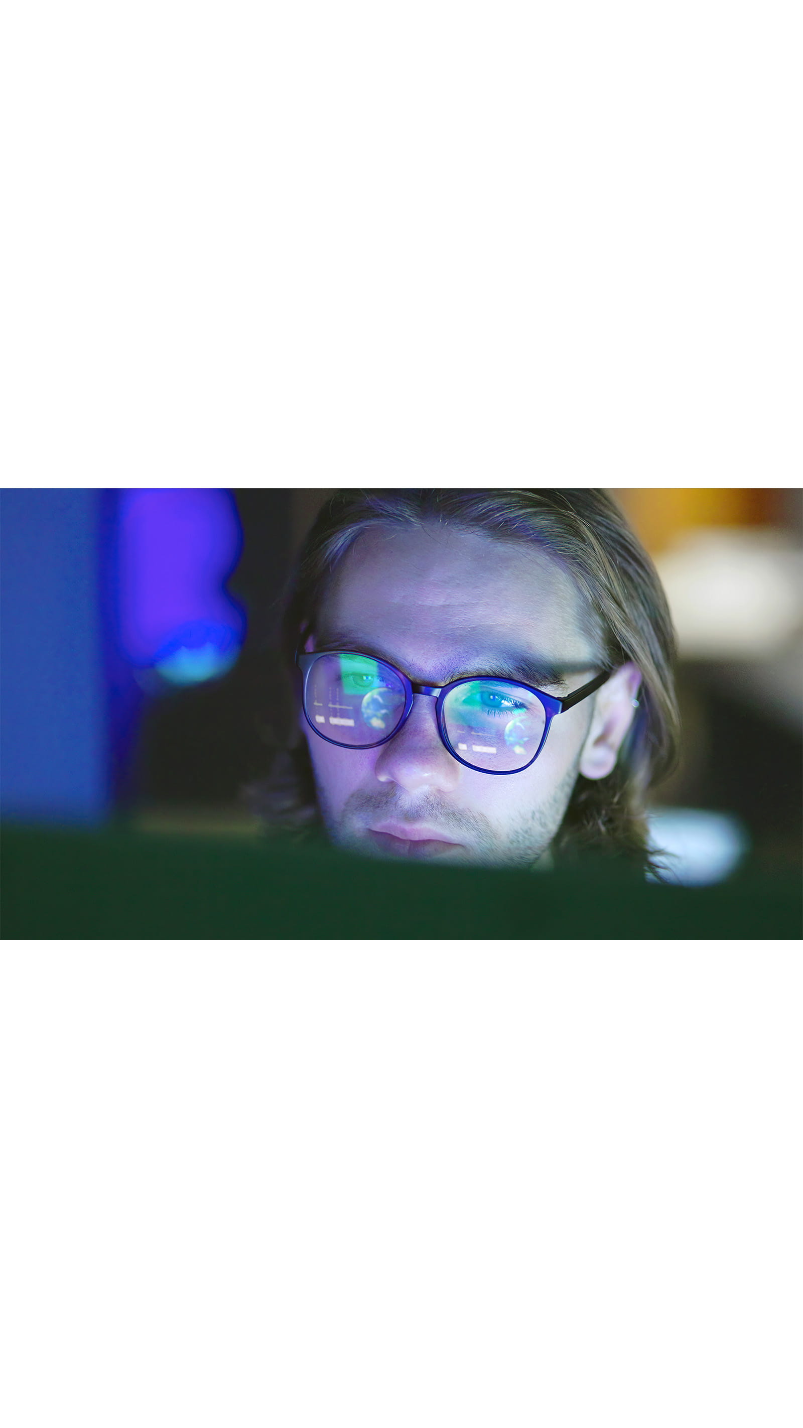 young man glasses reflecting computer screen dark room office