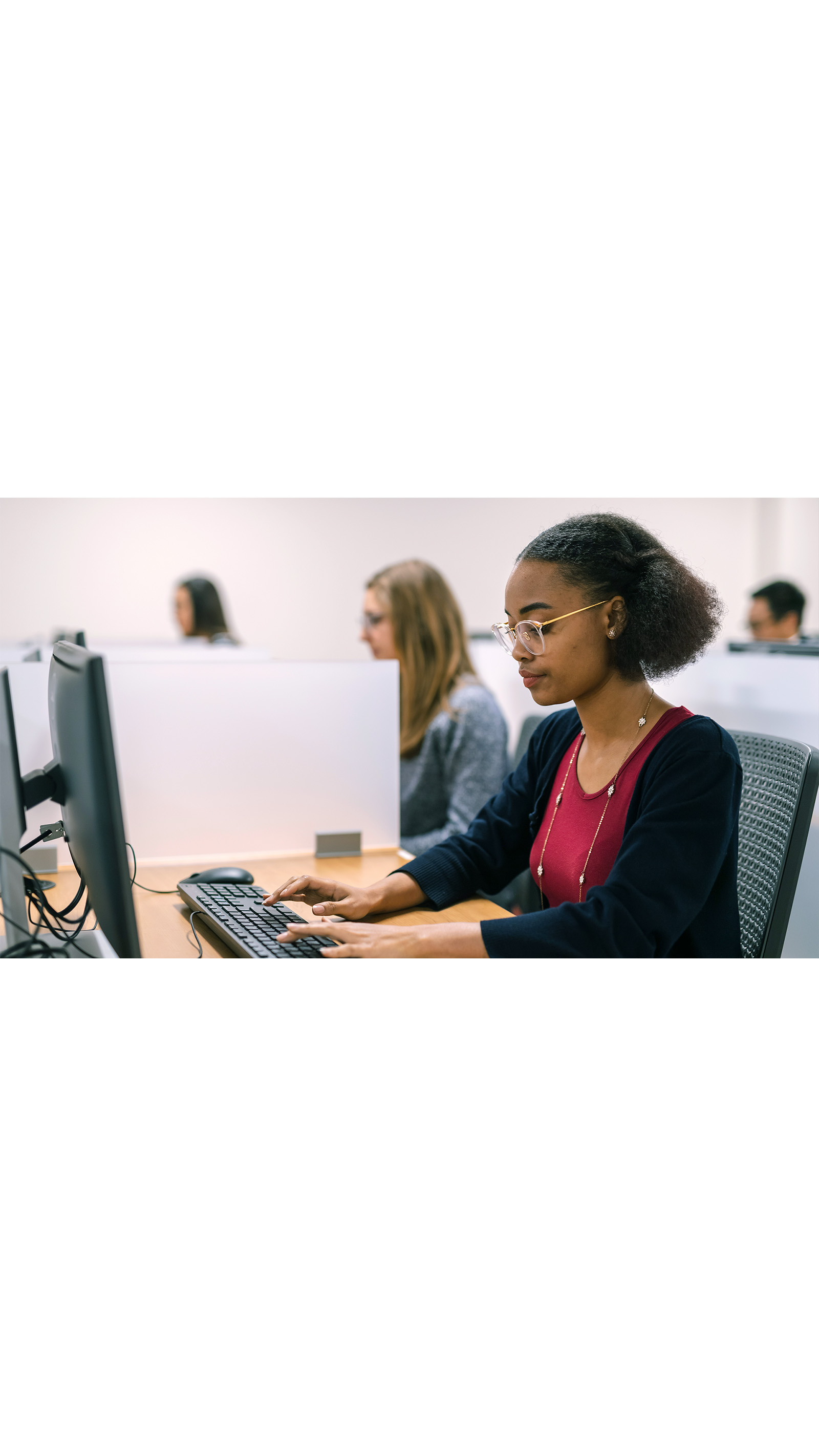 exam room young student black woman wearing glasses red top black cardigan sitting typing at a computer keyboard