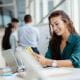 young woman employee working in an office smiling looking at mobile phone laptop desk