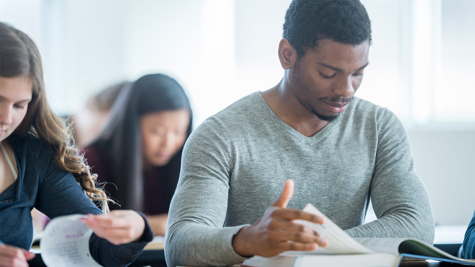 young students studying sitting in a classroom exams reading textbook turning page