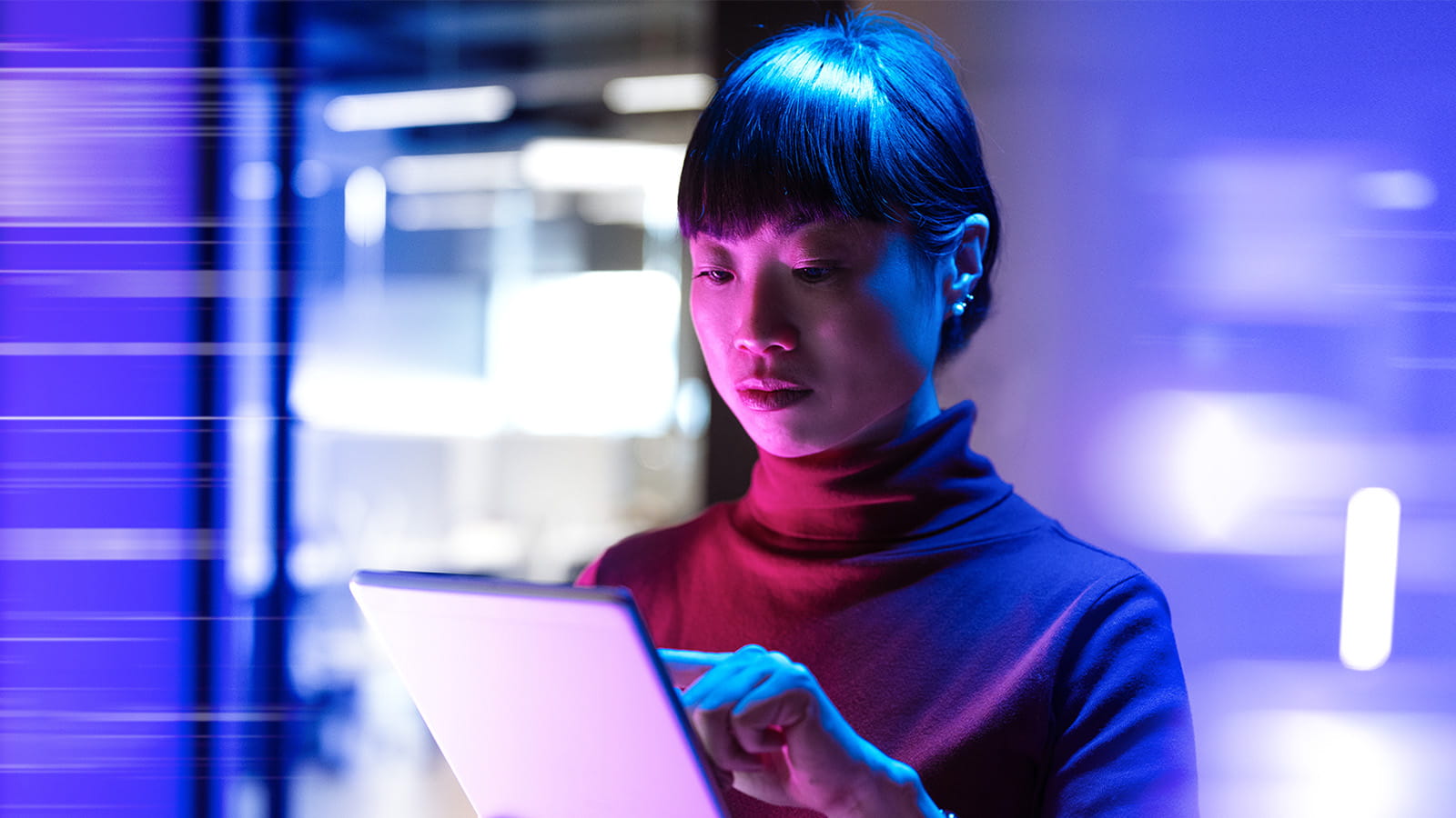 young asian woman holding using pointing at an electronic tablet in front of blurred blue lighting