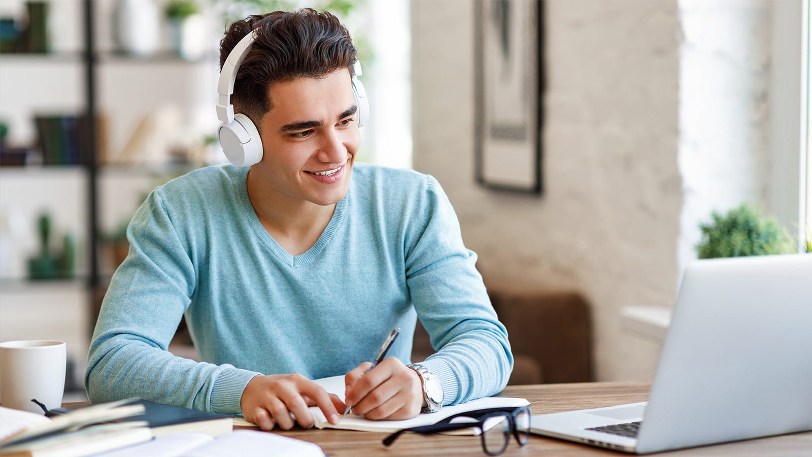 young man student studying looking at laptop wearing headphones writing taking notes