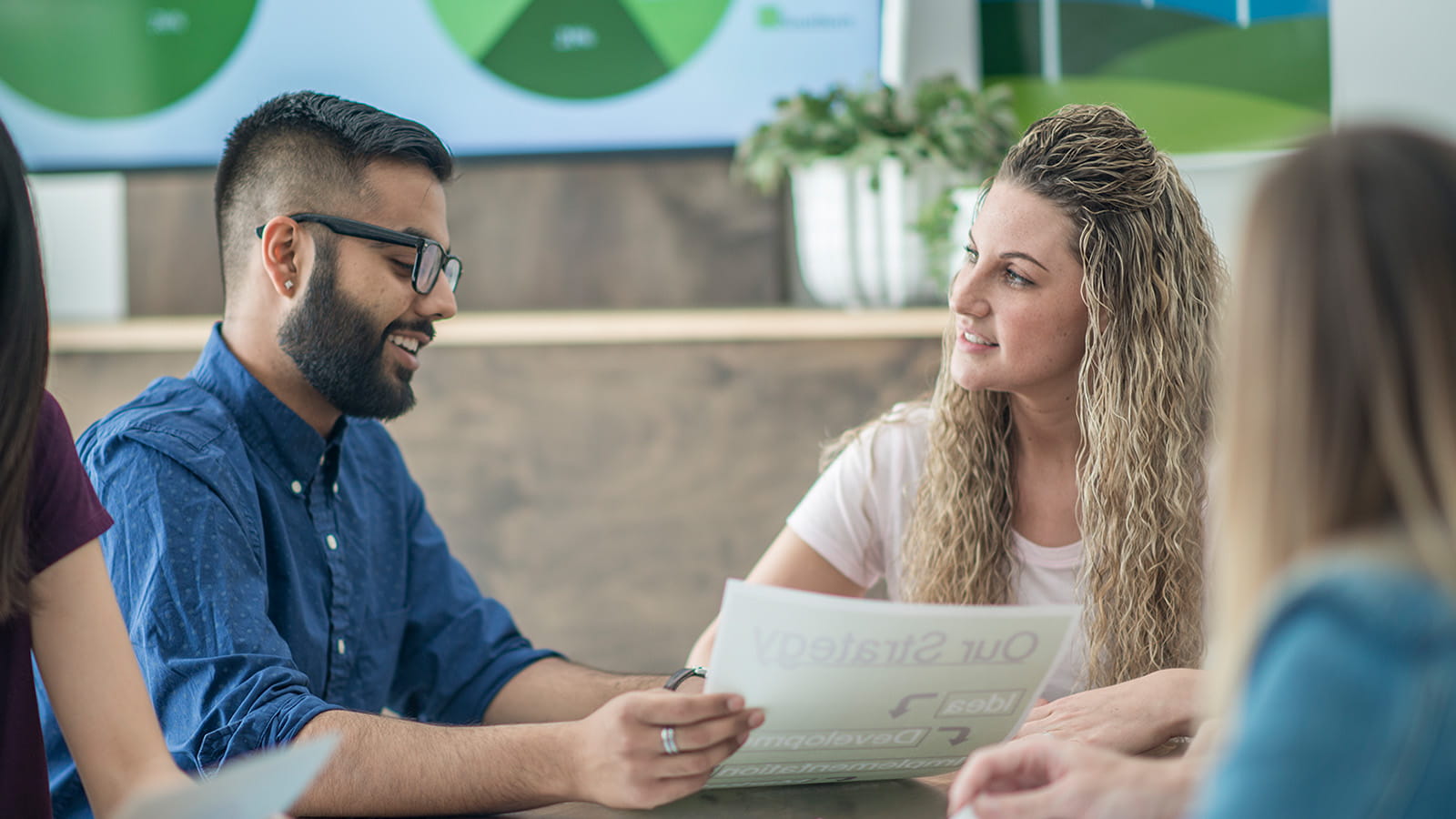 meeting office colleagues co-workers employees talking looking at paperwork charts graphs on screen