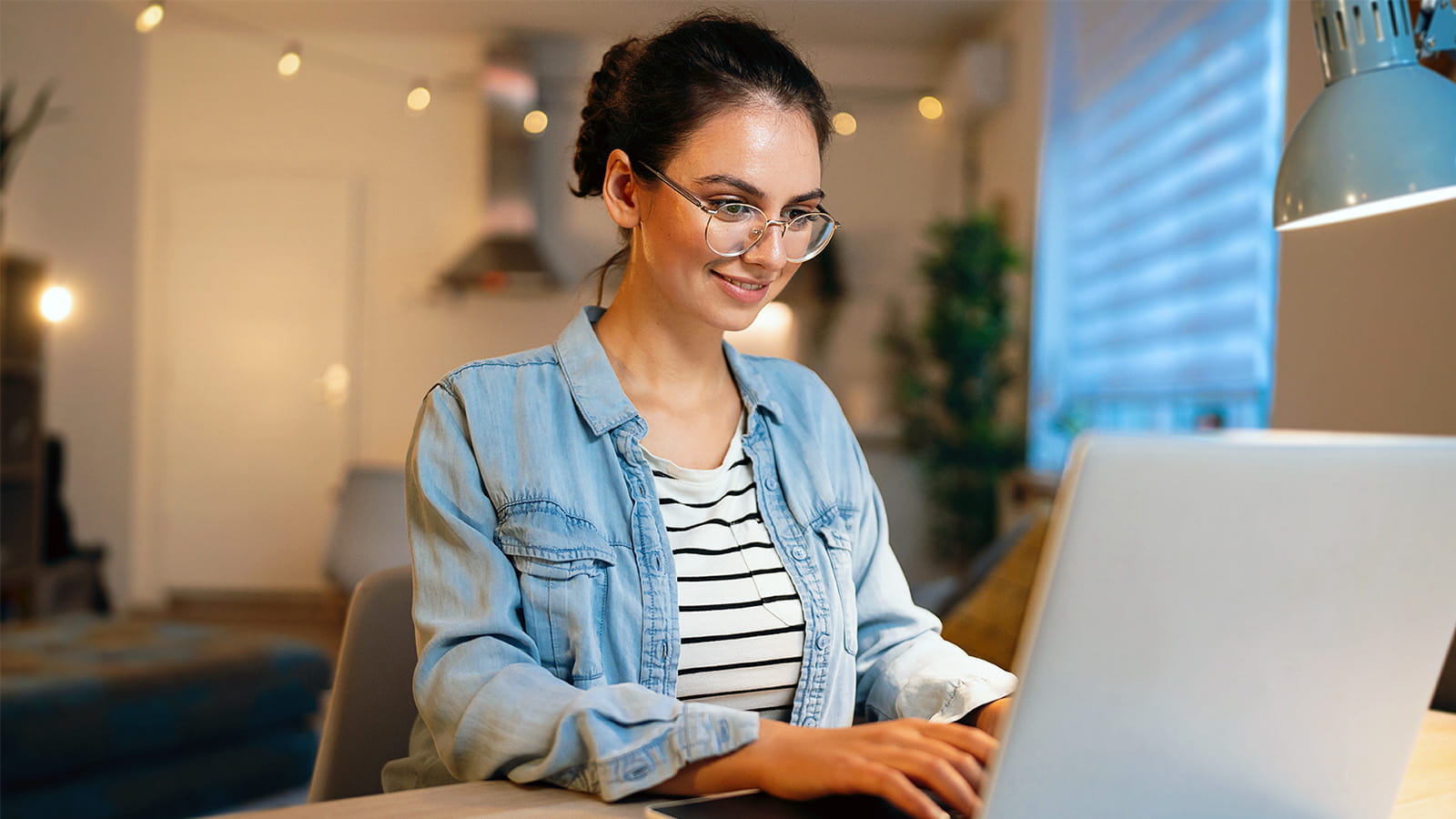 young woman student wearing glasses smiling typing on a laptop keyboard home office study