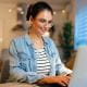 young woman student wearing glasses smiling typing on a laptop keyboard home office study