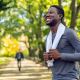 smiling young man jogger runner outside park green trees holding towel around neck