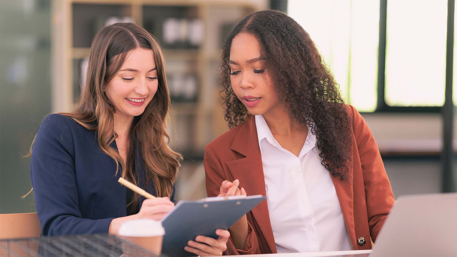 two women colleagues meeting working looking pointing at a tablet talking office