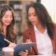 two women colleagues meeting working looking pointing at a tablet talking office