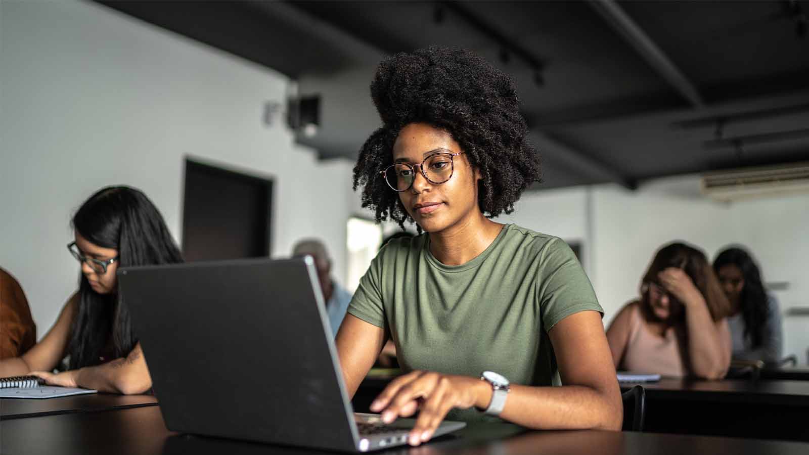 young woman student wearing glasses working on a laptop studying exams