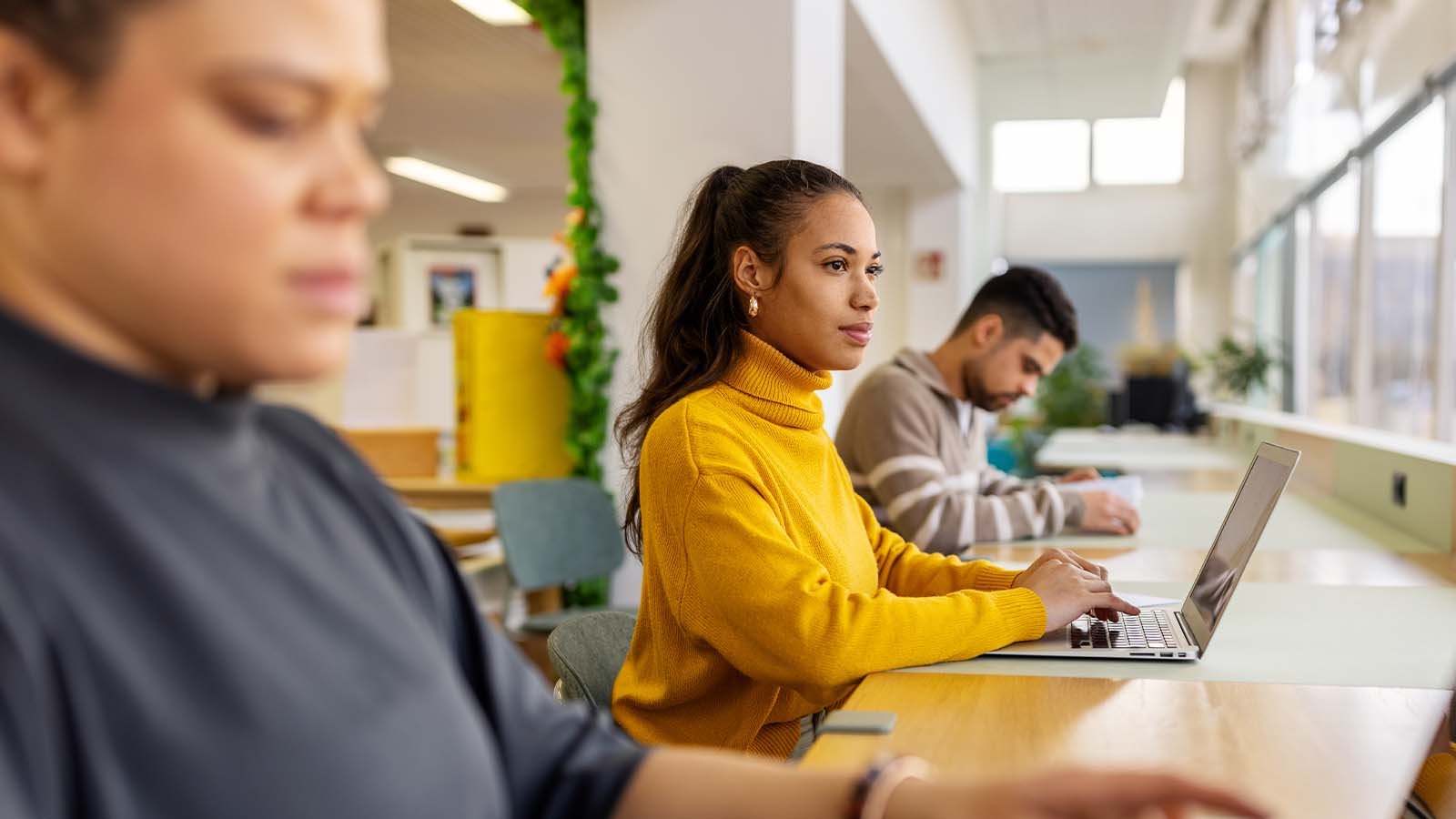 row of young people students working studying on laptops sitting at a desk