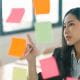 young woman employee working in an office meeting room pointing looking at post-it notes on glass
