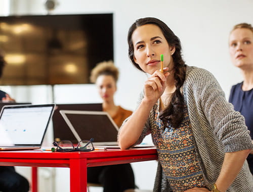 young woman student classroom sitting at a red desk with a laptop pointing to something with a pen