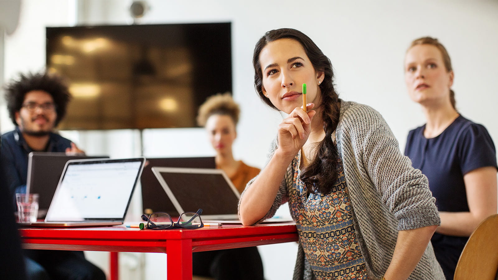 young woman student classroom sitting at a red desk with a laptop pointing to something with a pen