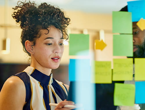 young woman employee working in an office meeting room planning post it notes on glass
