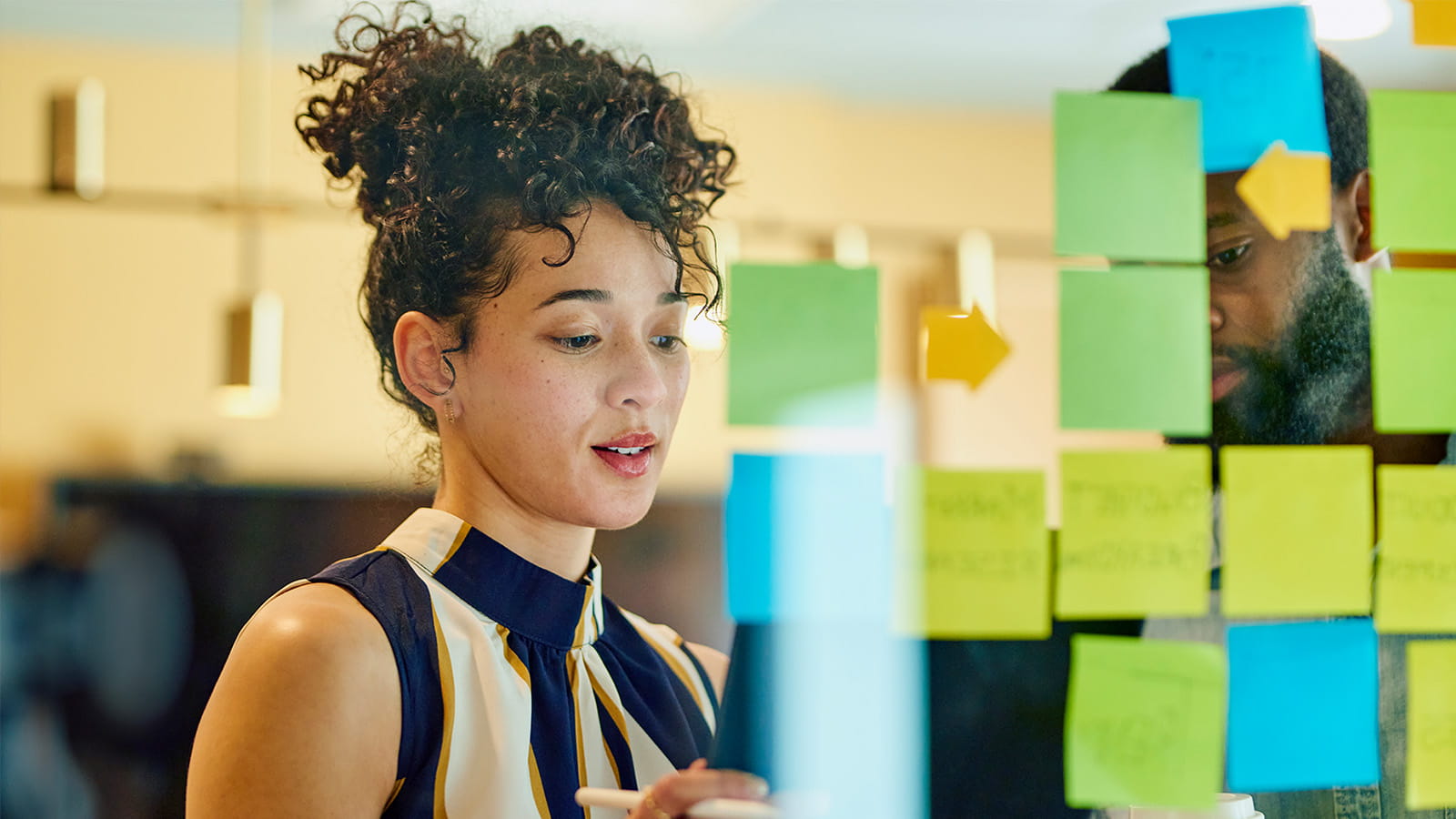 young woman employee working in an office meeting room planning post it notes on glass