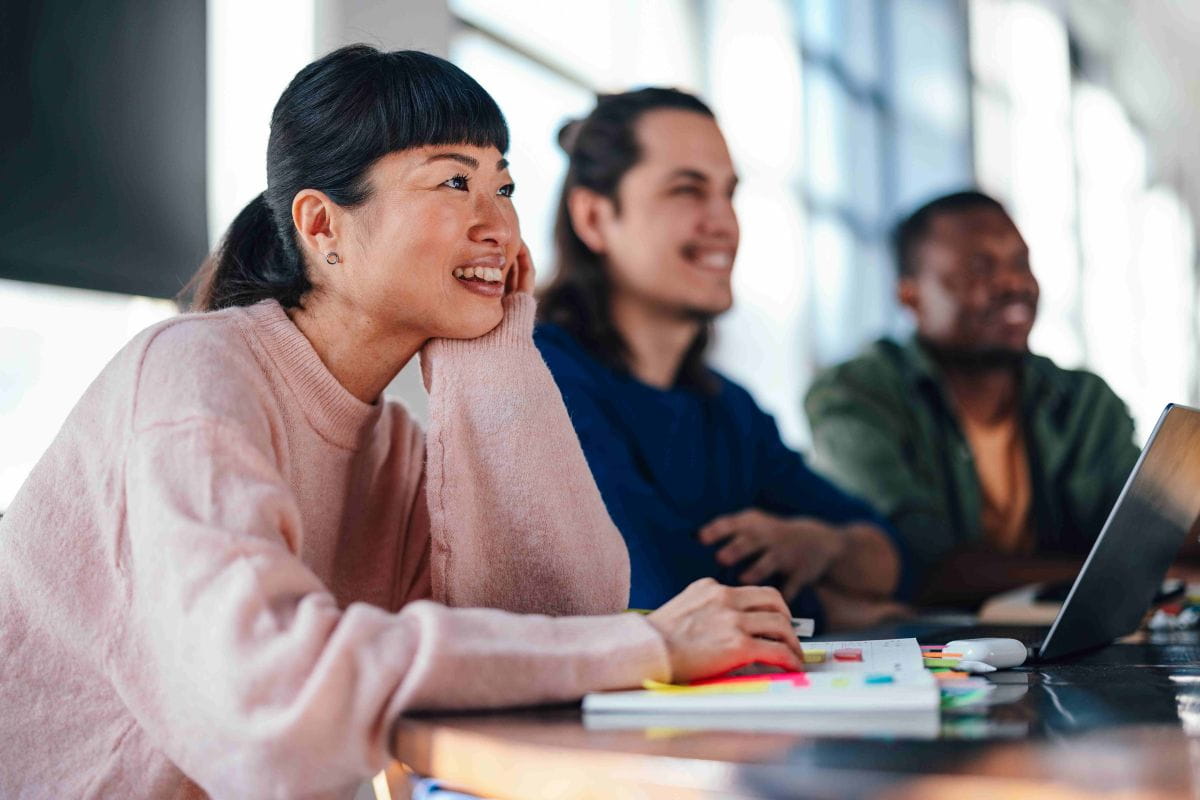 Group of three smiling students with paper notes and laptop