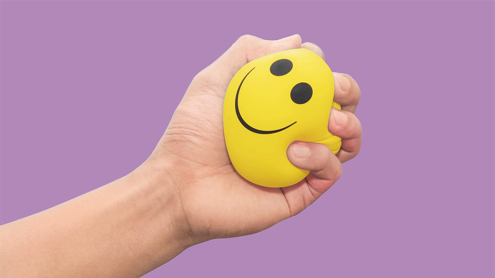 yellow stress ball smiley face held squeezes in a hand purple background