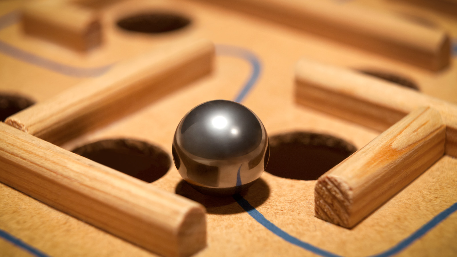 silver marble sitting on a wooden board maze game between two holes on a blue line