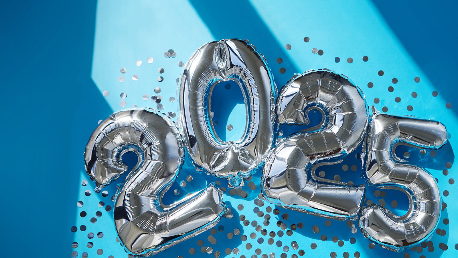 silver 2025 helium ballons laying on a blue floor with confetti