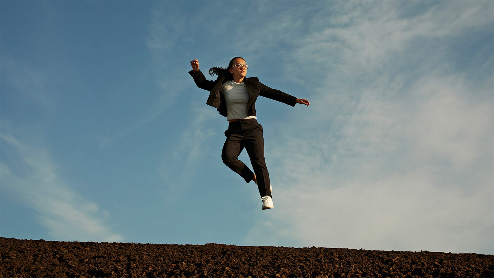 photo of a woman jumping high with blue sky and clouds behind