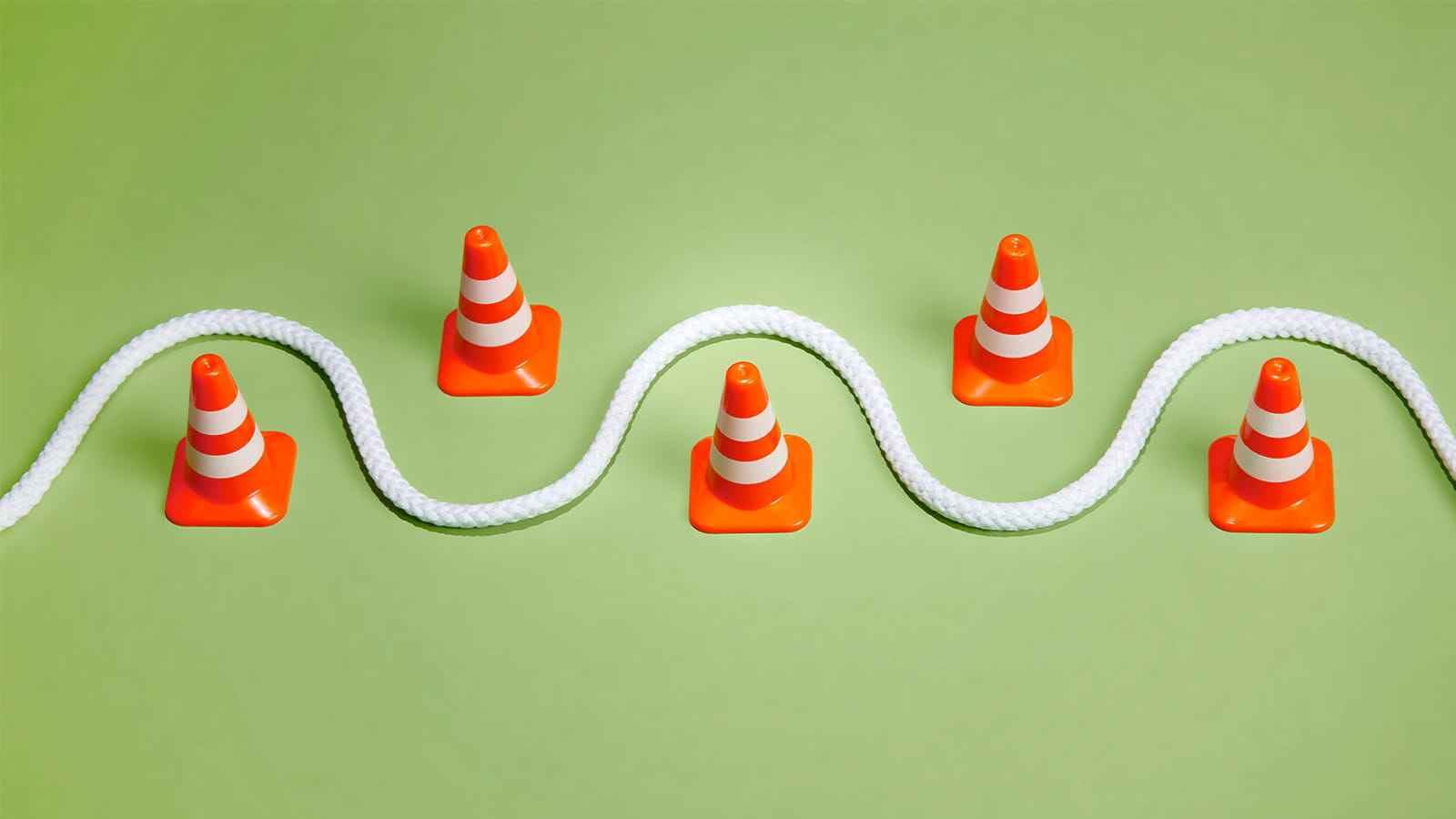 staggered line of orange traffic cones with a white rope swerving wave in between them green background