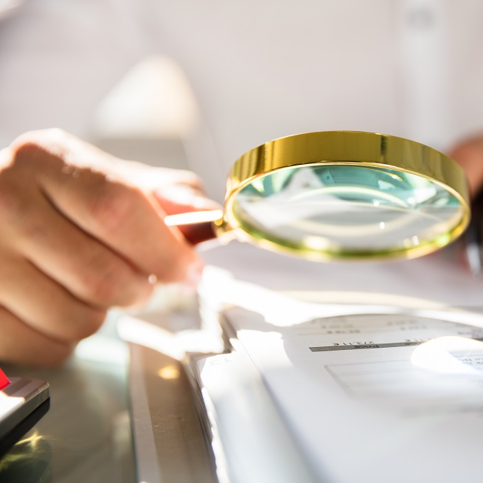 Person holding a magnifying glass over papers