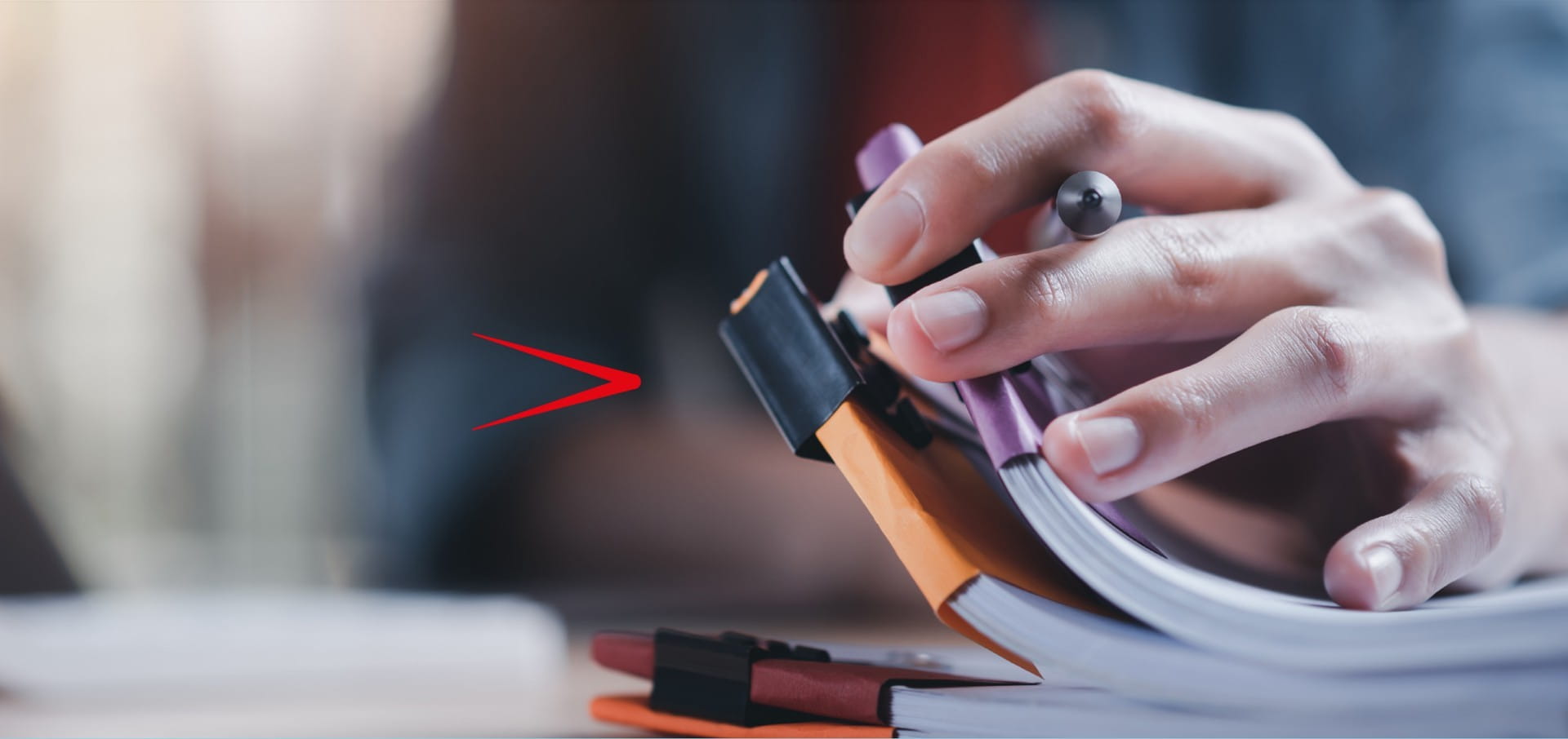 Close up of hand holding a pen and flicking through three lots of paperwork grouped together with coloured clips