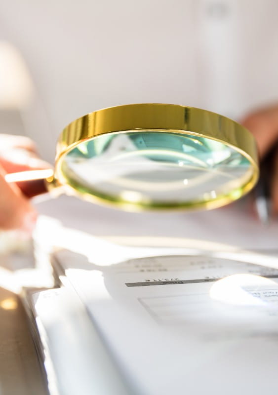 Close up of brass magnifying glass being used to examine writing on paper.