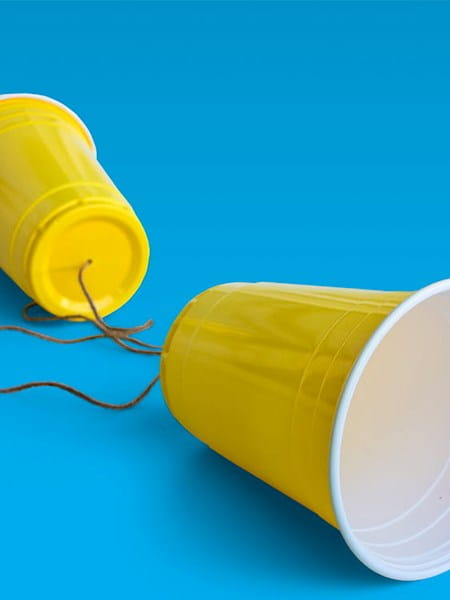 yellow plastic cups string between telephone talk blue background