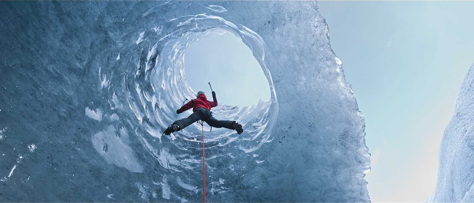 ice climber climbing man orange hoodie black trousers helmet pick blue ice cave