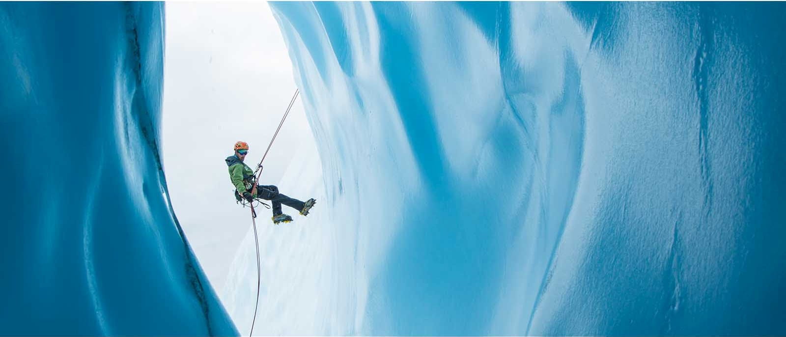 ice climber climbing man green hoodie black trousers helmet pick blue ice cave