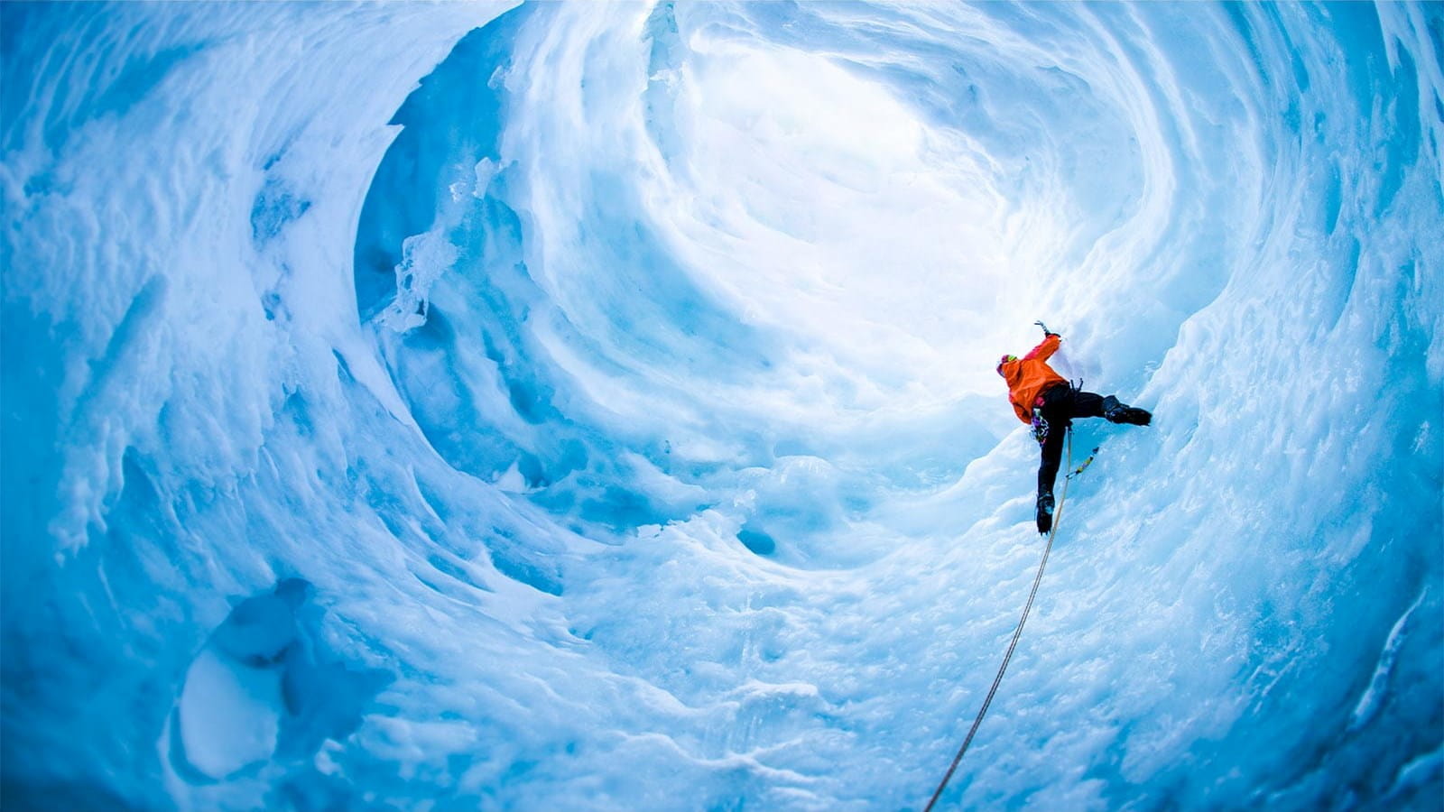 ice climber climbing man orange hoodie black trousers helmet pick blue ice cave