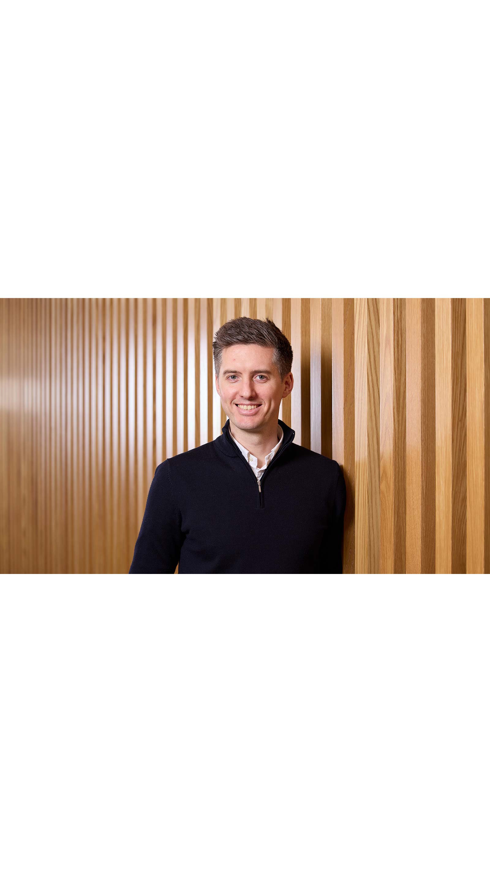 Liam May, director at NorthEdge, man standing in front of wooden panels