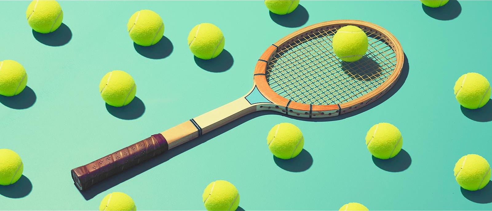 tennis racket laying on ground with multiple yellow tennis balls teal background
