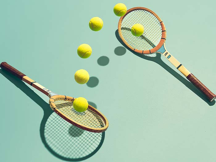 two tennis rackets laying on ground hitting multiple yellow tennis balls between each other teal background