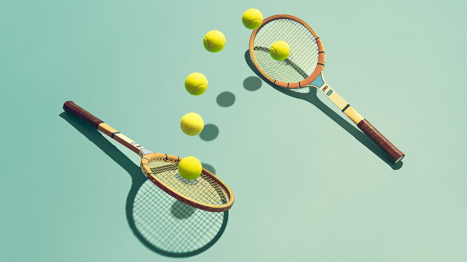 two tennis rackets laying on ground hitting multiple yellow tennis balls between each other teal background