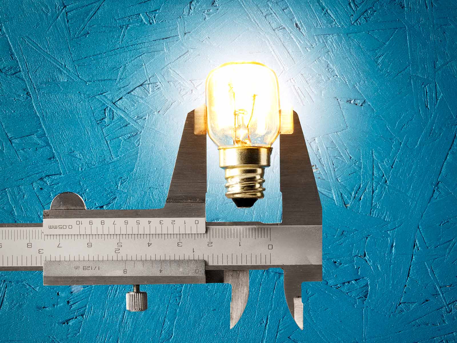 light bulb glowing being held by a vernier caliper clamp ruler measuring blue background