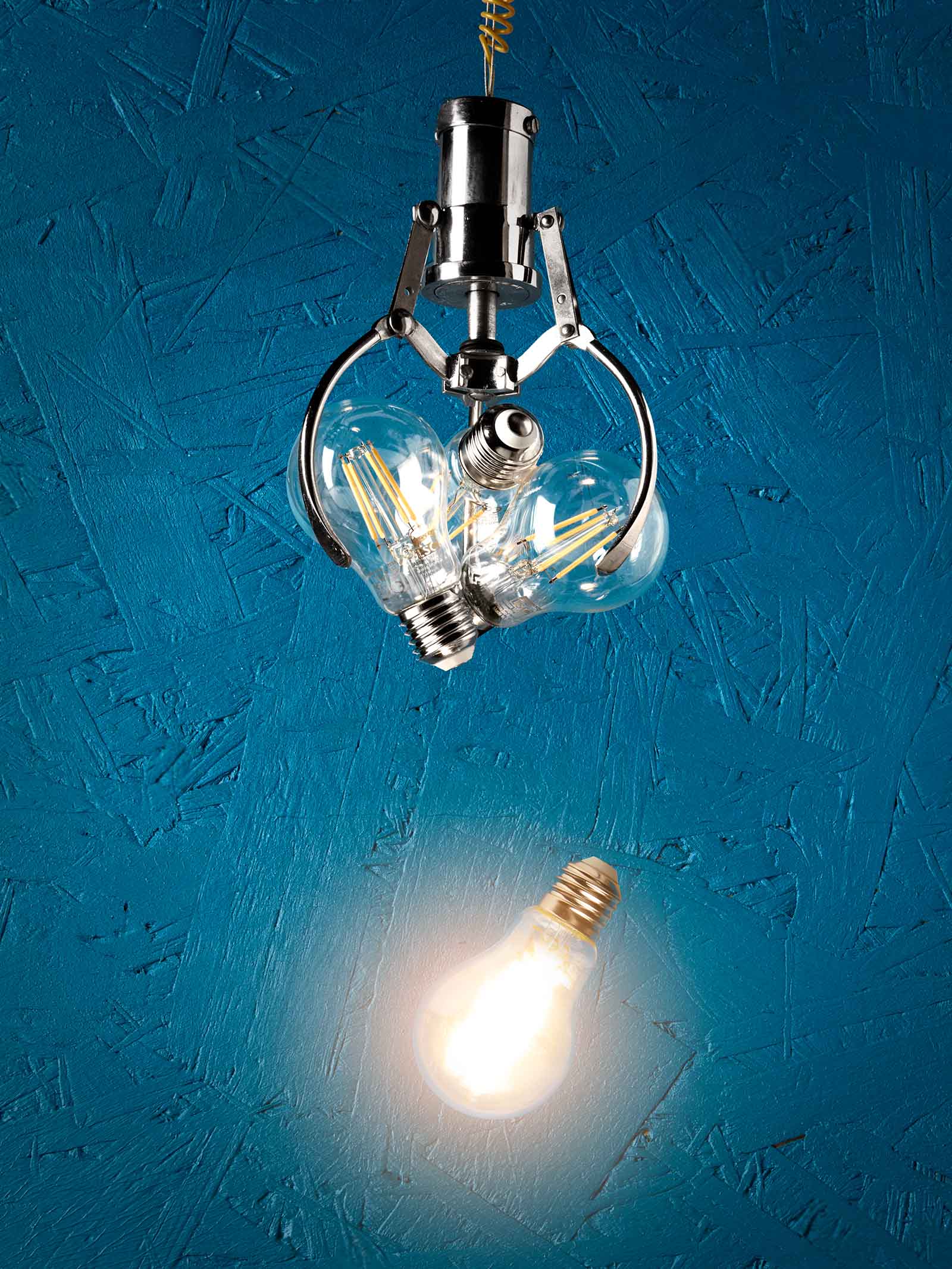 light bulb glowing falling from an arcade claw bulbs blue background