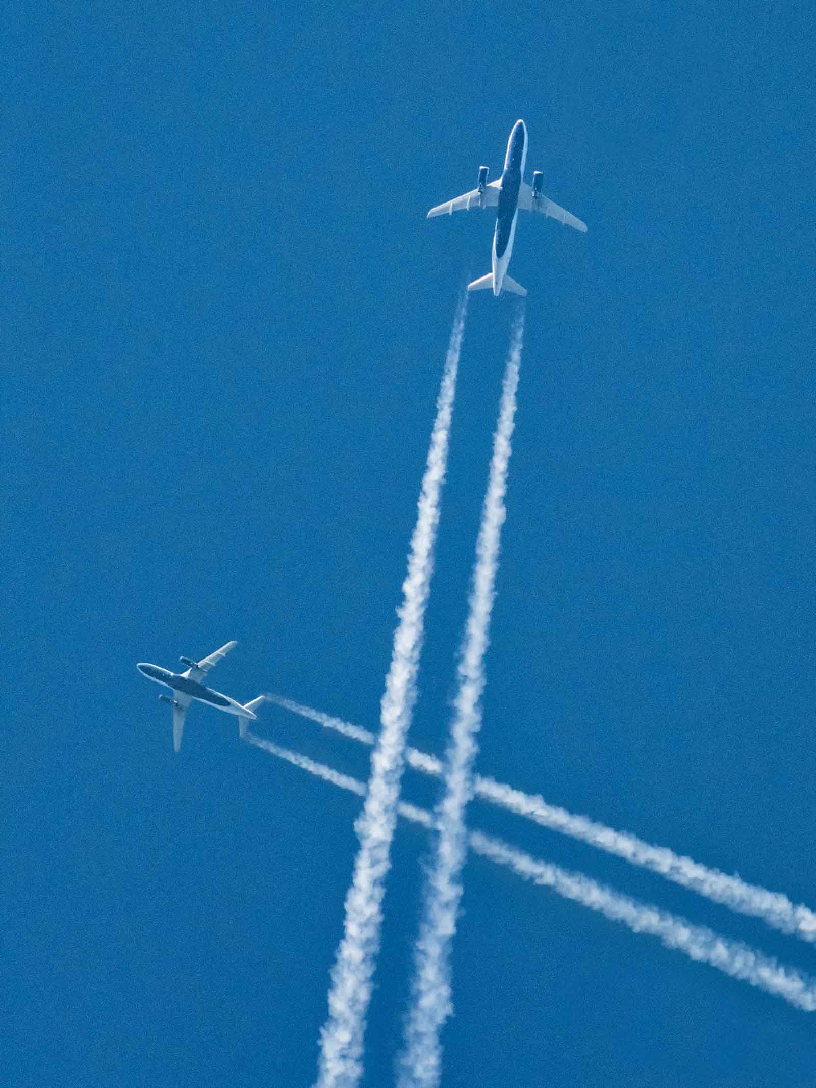 two airplanes jet streams passing each other seen from below blue sky