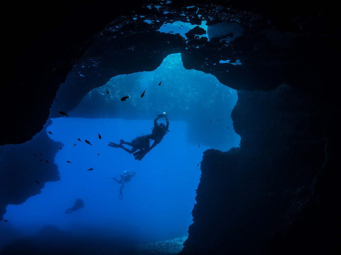 deep sea scuba diver swimming in a dark underwater cave blue