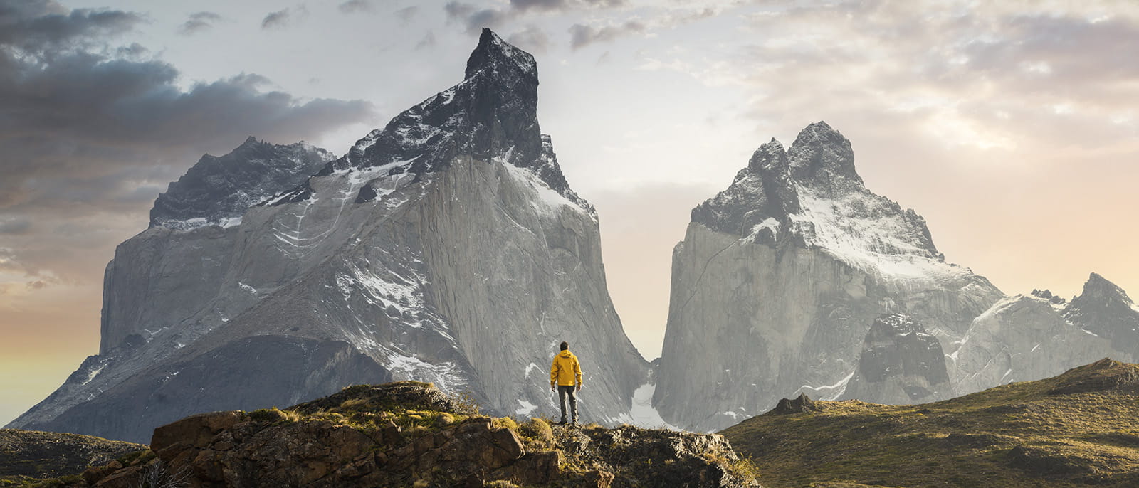 Climber standing on a cliff in front of two mountain peaks snow-capped