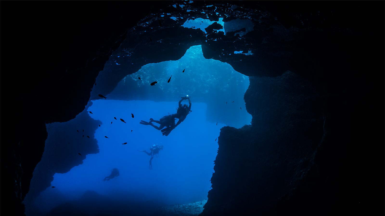 deep sea scuba diver swimming in a dark underwater cave blue