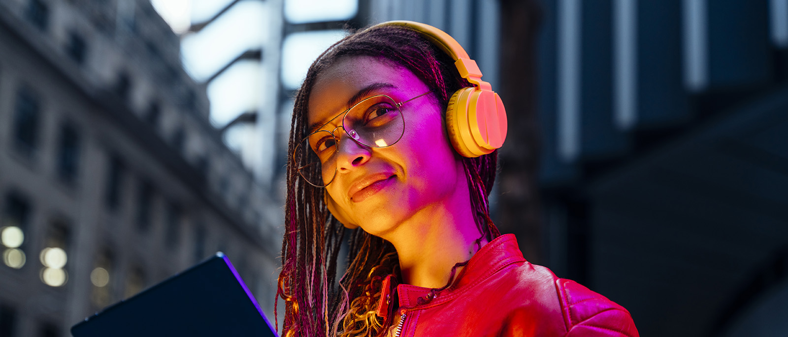 young woman wearing orange headphones with orange and pink light from an electronic tablet