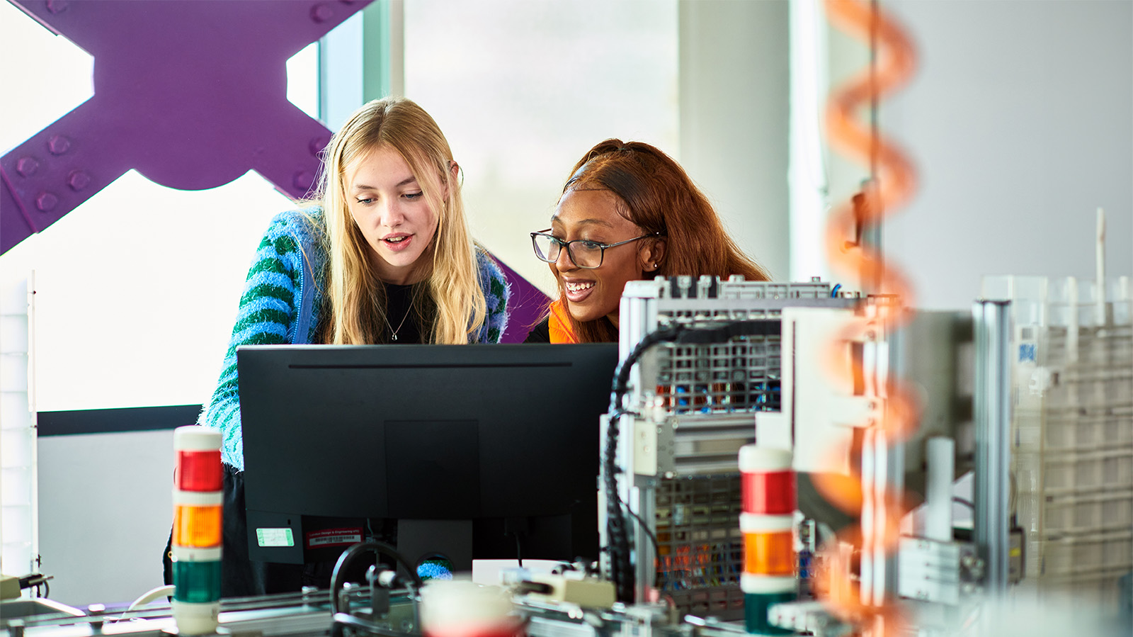 two young women colleagues employees talking looking at a computer monitor screen science lab