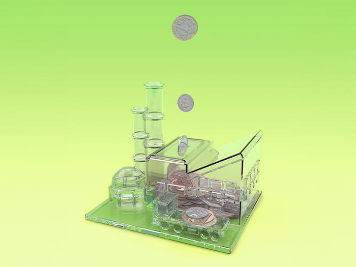 GBP coins falling into a plastic money box bank in the shape of a factory on a green background