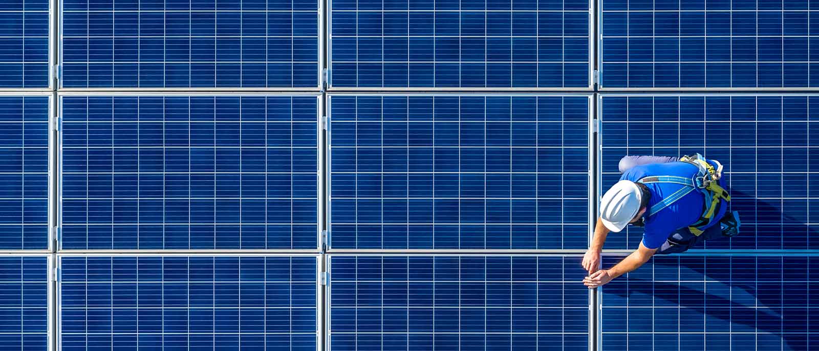 aerial shot photo of an electrician man wearing a white hard hat installing solar panels