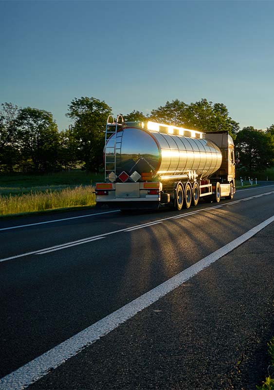 photo of an oil truck driving on a road at sunset sun setting over a field long grass blue sky