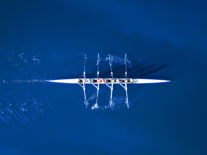 birds eye aerial view of rowing boat team four athletes blue water