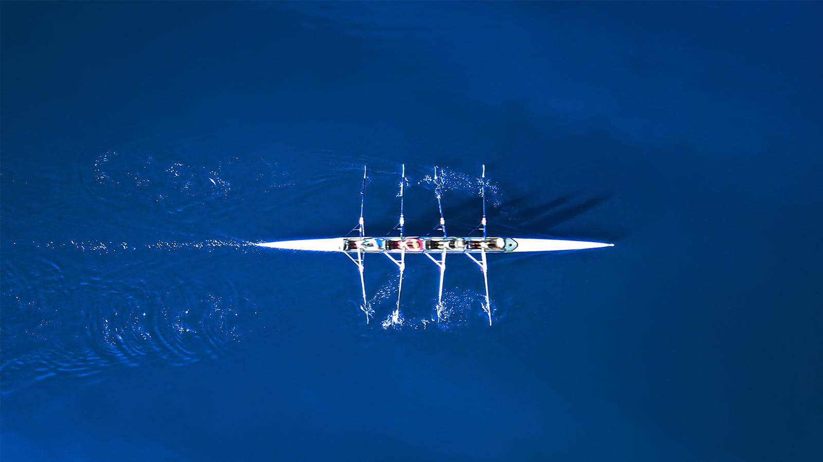 birds eye aerial view of rowing boat team four athletes blue water