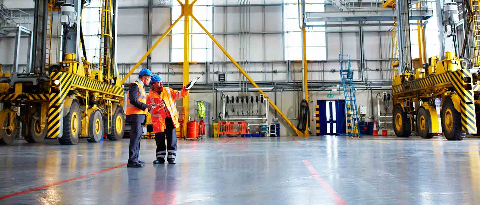 Shot of two warehouse workers talking together over a clipboard inside of a large warehouse high vis hard hats
